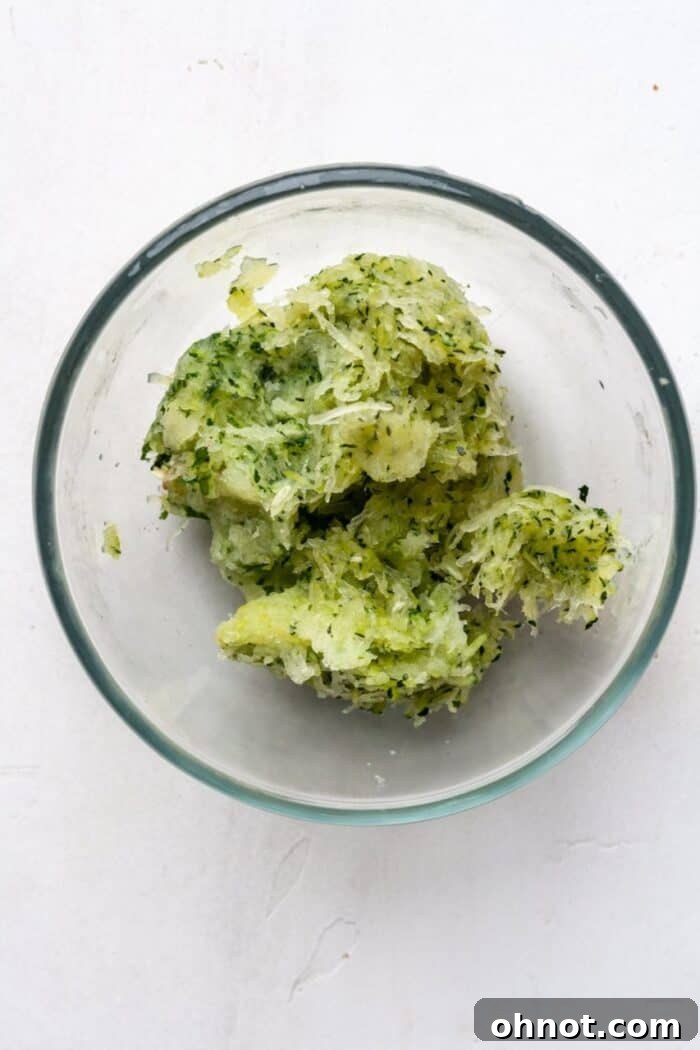 Finely grated zucchini in a clear glass bowl, showcasing its texture after all excess water has been squeezed out.