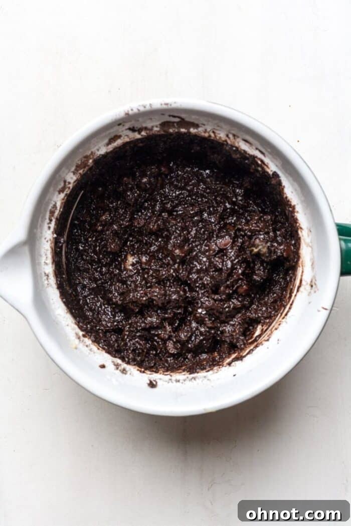 The rich Paleo chocolate muffin dough in a bowl, with vibrant grated zucchini and generous dark chocolate chips lovingly folded in.
