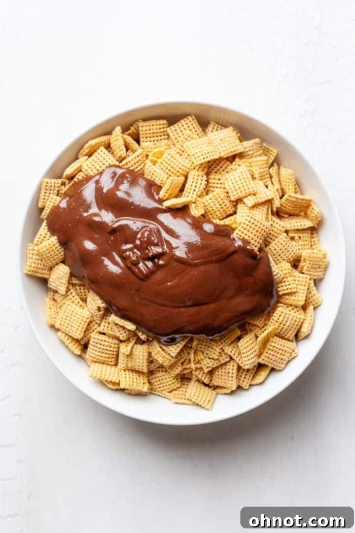 Chex mix cereal being coated with melted chocolate and peanut butter mixture in a large bowl.