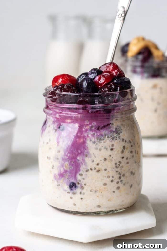 A close-up of oatmeal with frozen fruit and peanut butter in a glass jar