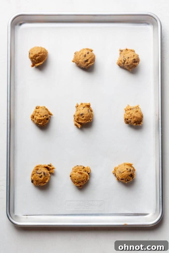 Pumpkin cookie dough balls neatly arranged on a baking pan lined with parchment paper.