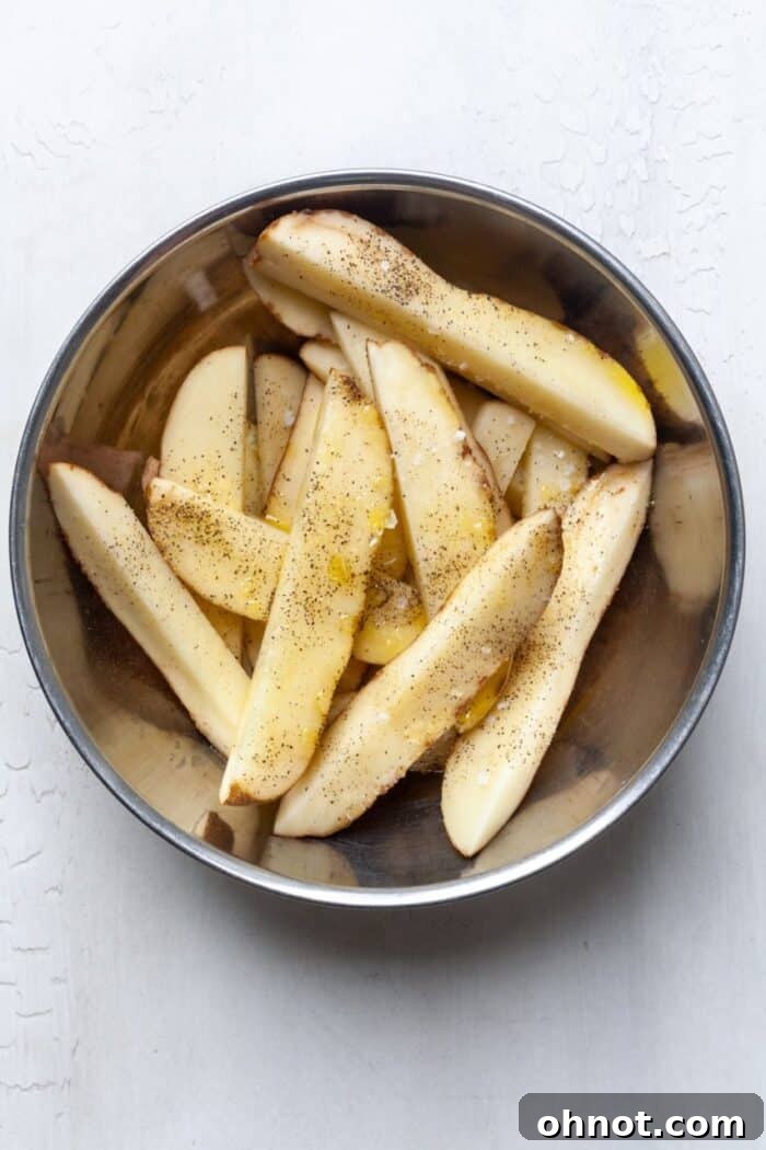 Sliced potatoes in bowl with oil and seasoning