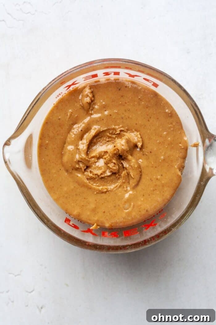Close-up of creamy natural peanut butter being measured in a cup, highlighting its smooth texture