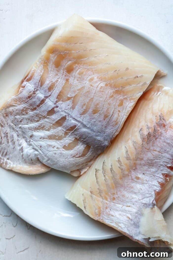 Raw Chilean sea bass filet on a white plate, ready for seasoning.