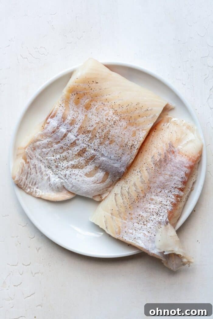 Seasoned Chilean sea bass filet on a plate with visible salt and pepper.