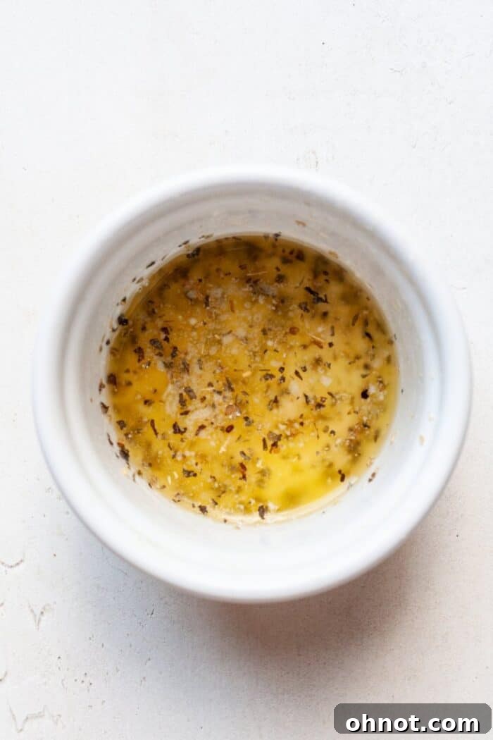 Small bowl containing melted butter, minced garlic, and oregano.