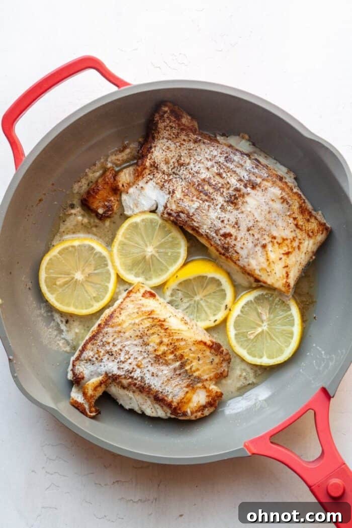 Pan-seared fish flipped, covered with lemon-garlic butter sauce, and lemon slices in the skillet.