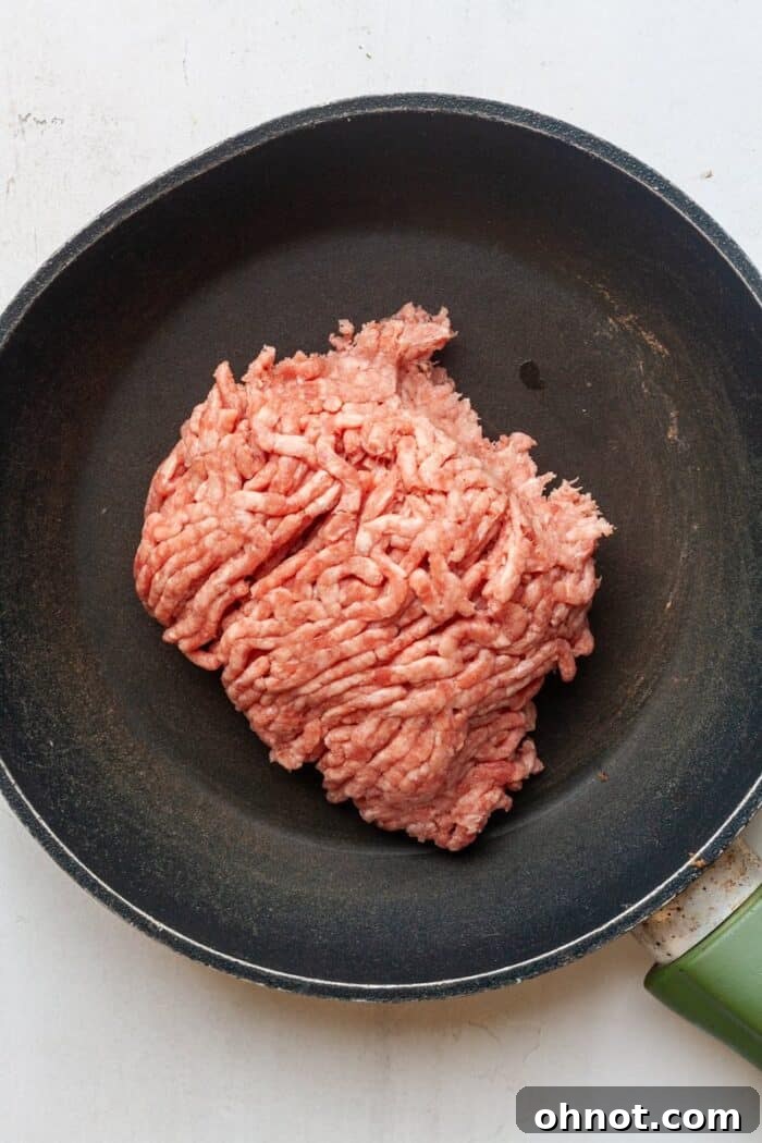 Ground beef cooking in a skillet, being broken apart with a spatula to create crumbles.