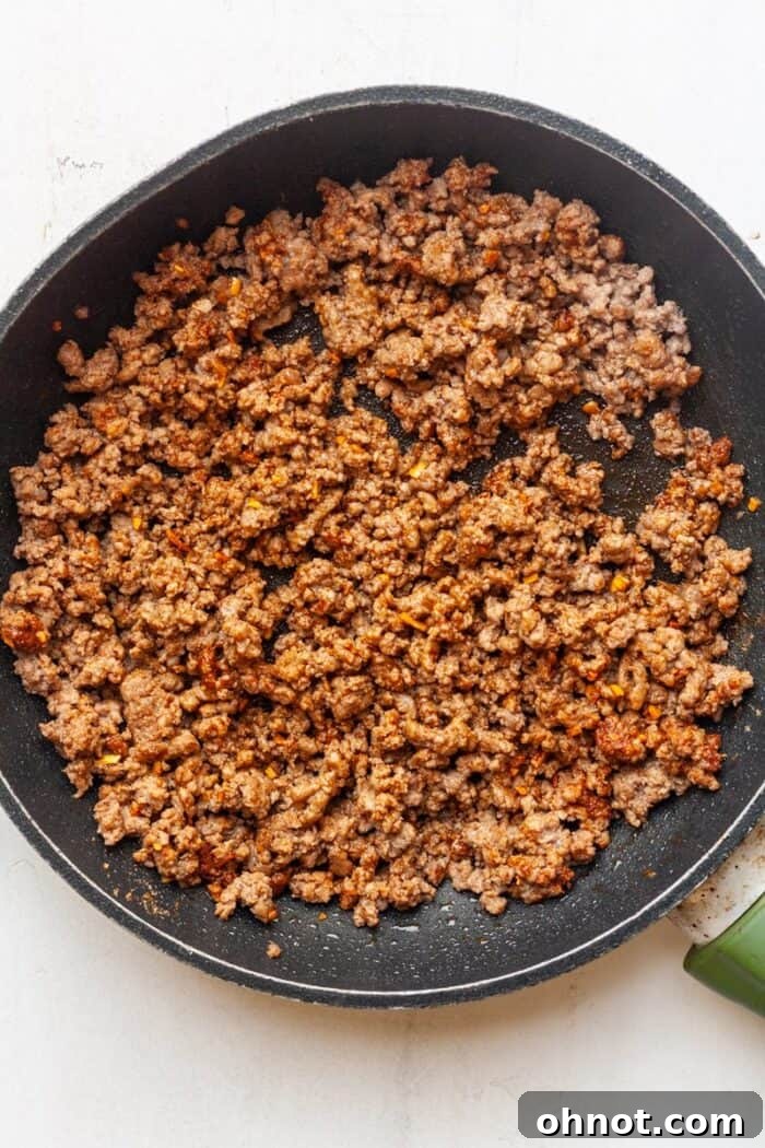 Taco beef simmering with water and a blend of vibrant seasonings in a skillet, absorbing flavors.