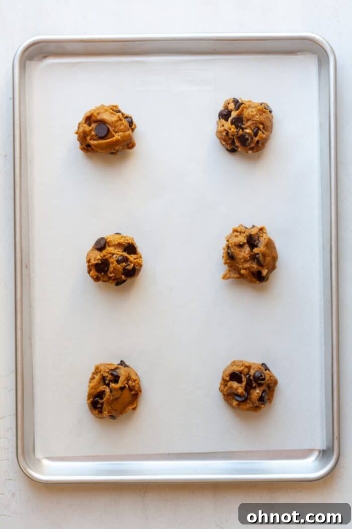 Scooped cookie dough balls arranged on a parchment-lined baking pan, ready for the oven.