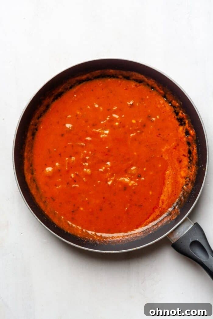 Tomato sauce and coconut milk being stirred together in a skillet