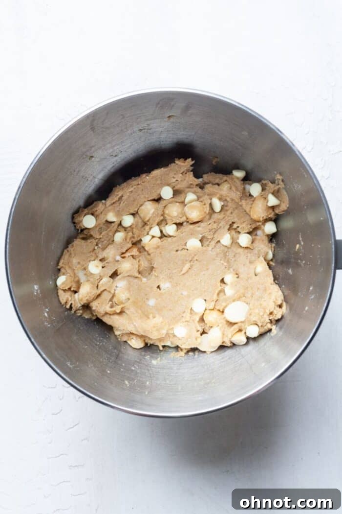 Vegan cookie dough in a bowl with white chocolate chips and macadamia nuts folded in.