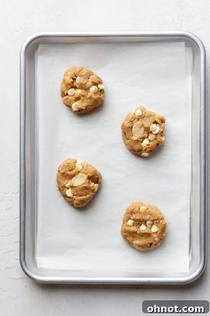 Unbaked white chocolate macadamia nut cookies, scooped and slightly flattened on a parchment-lined baking pan.