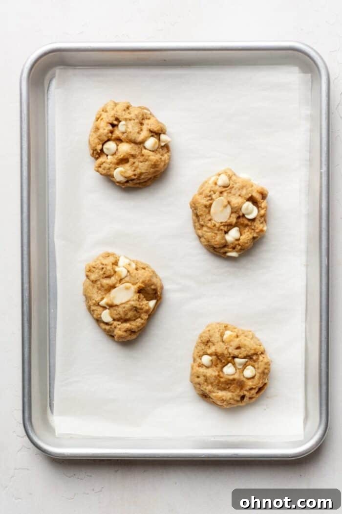 Freshly baked vegan white chocolate macadamia nut cookies cooling on the pan, showing golden edges.