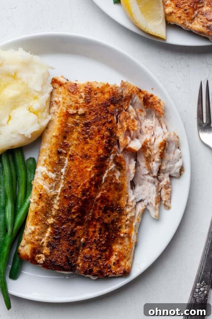 A serving of flaky blackened mahi mahi on a white plate, showing its perfectly cooked interior.