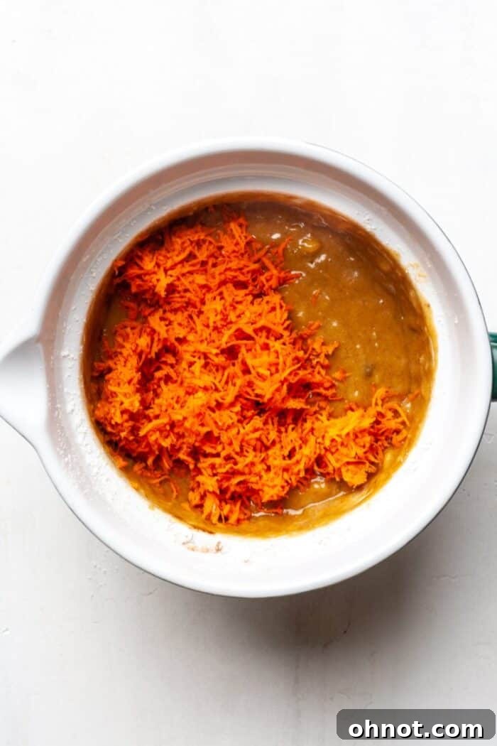 Carrot muffin batter in a bowl, carrots being folded in.