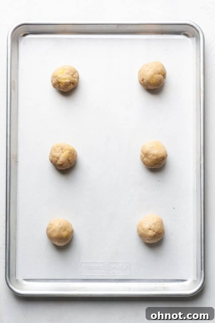 Portioned gluten-free lemon cookie dough balls on a parchment-lined baking sheet, garnished with lemon zest.