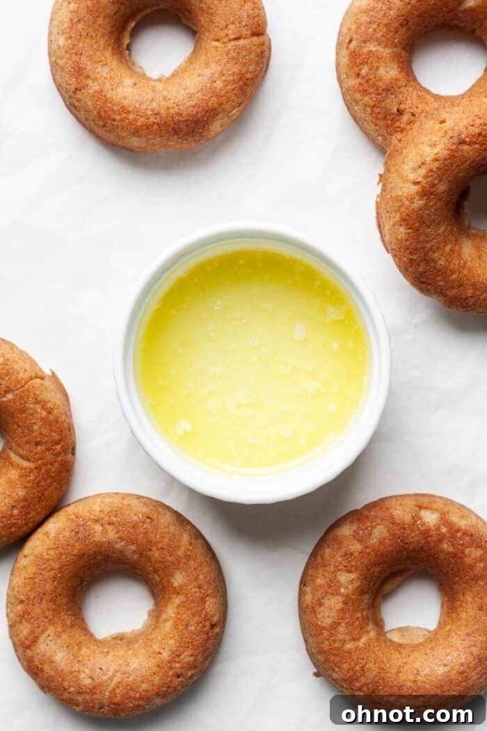 Melted butter in a bowl next to warm donuts, ready for coating