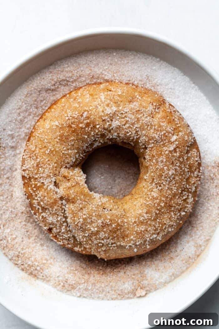A buttered donut being coated in cinnamon sugar mixture, showing full coverage