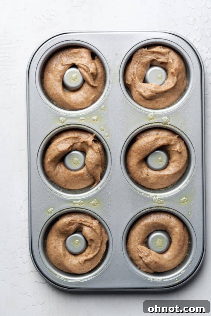 Donut batter piped evenly into a greased donut pan, filling each cavity just right