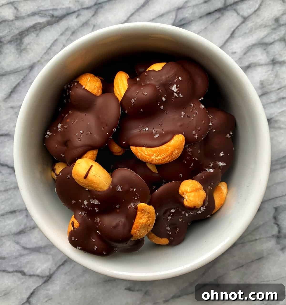 Close-up of three finished chocolate cashew clusters sprinkled with sea salt, ready to be eaten.
