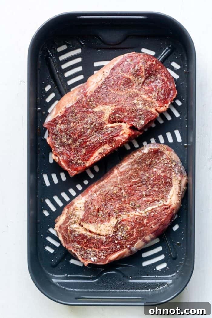 Two seasoned ribeye steaks carefully placed in an air fryer basket, ready for cooking