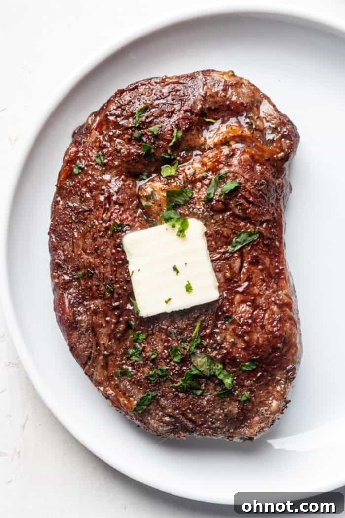 Air fryer ribeye steak topped with melting butter and fresh herbs, ready for serving