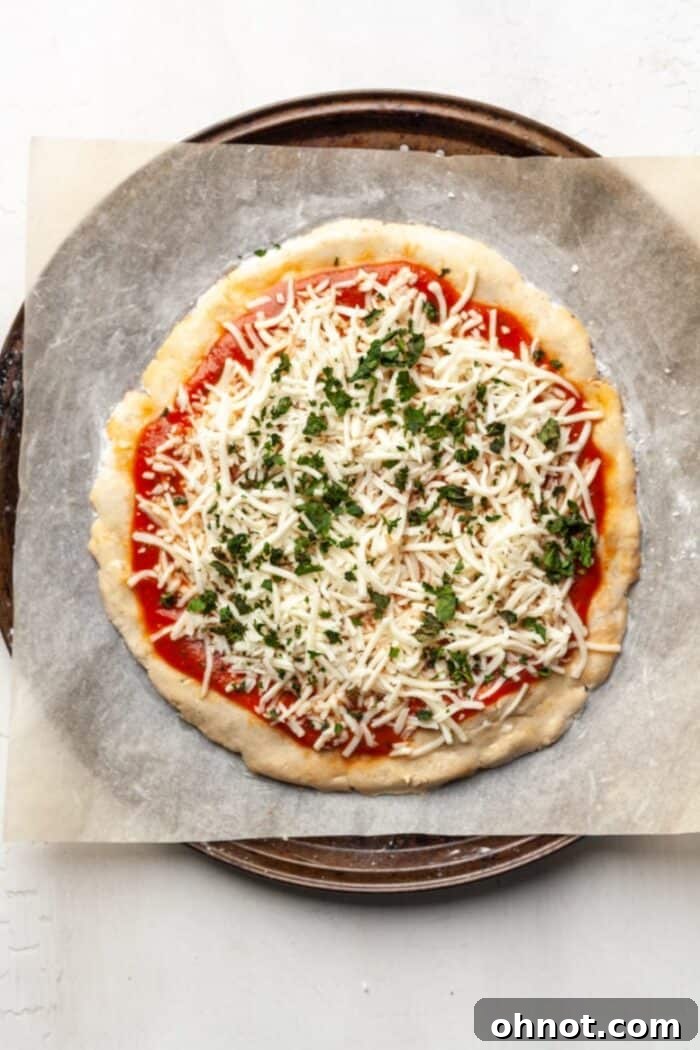 Dairy-free cheese being sprinkled over a partially baked Paleo pizza crust.