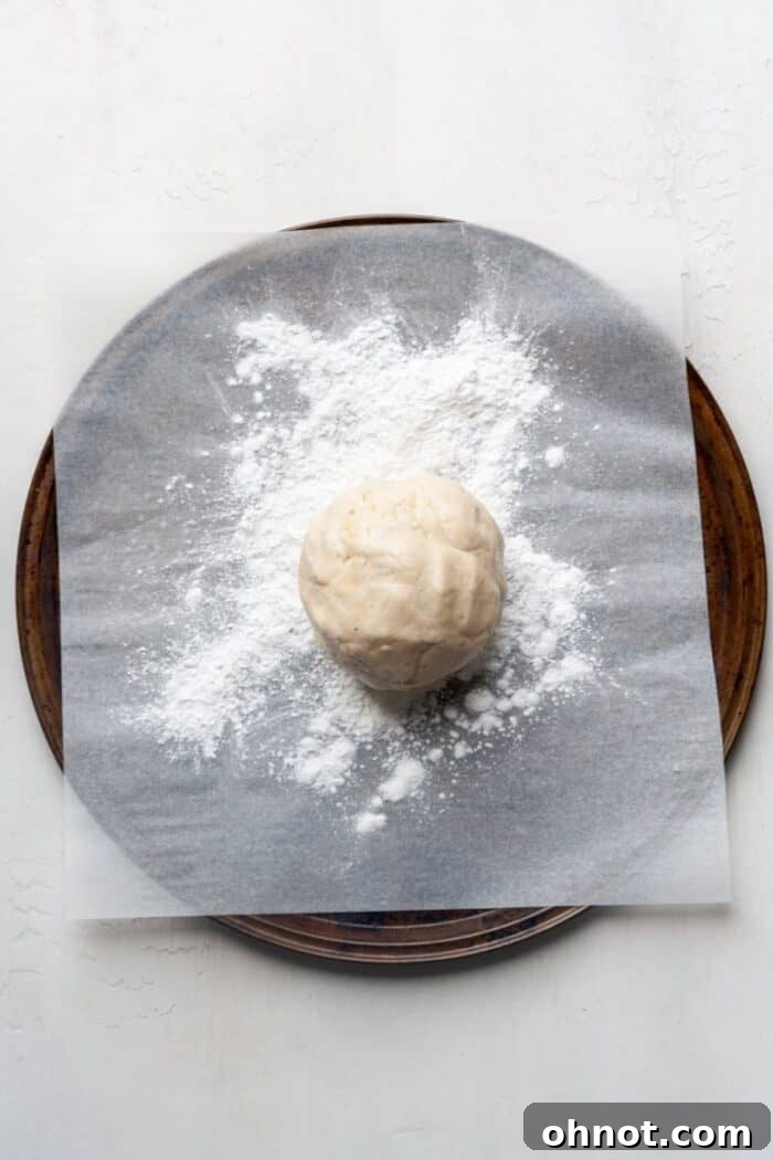 A round ball of gluten-free pizza dough placed on a tapioca flour-dusted pan, ready for shaping.