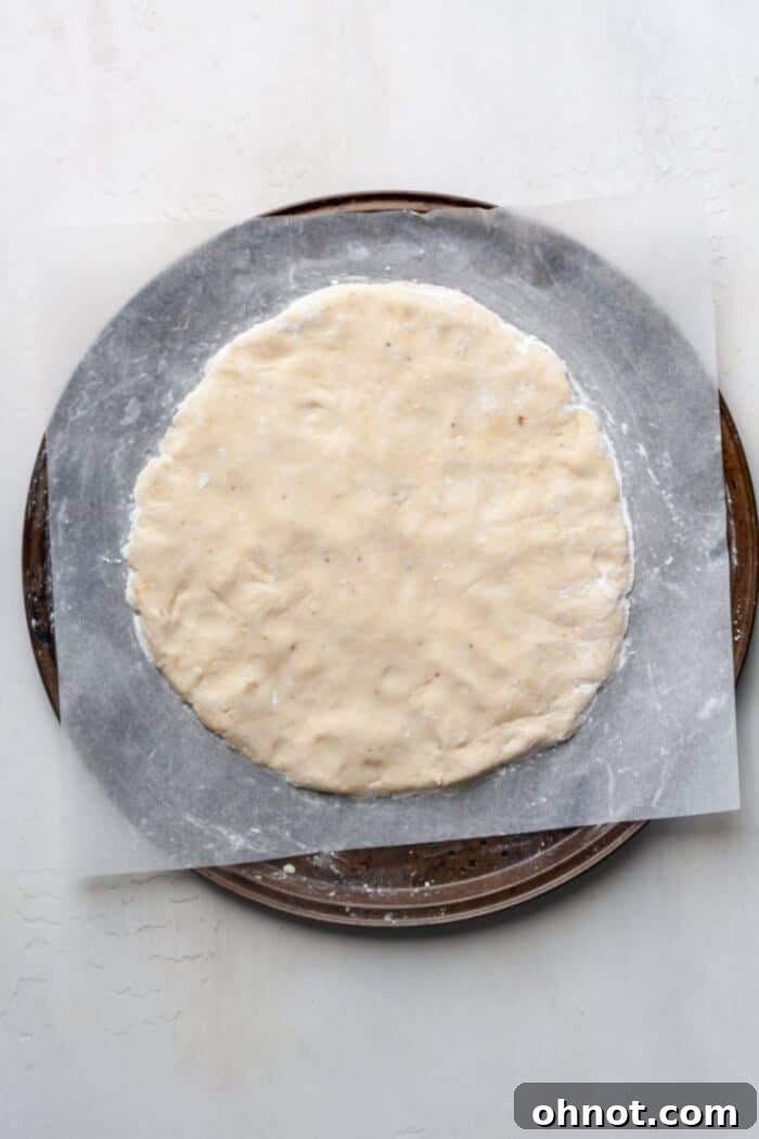 A perfectly shaped gluten-free, dairy-free pizza crust spread evenly on parchment paper, ready for baking.