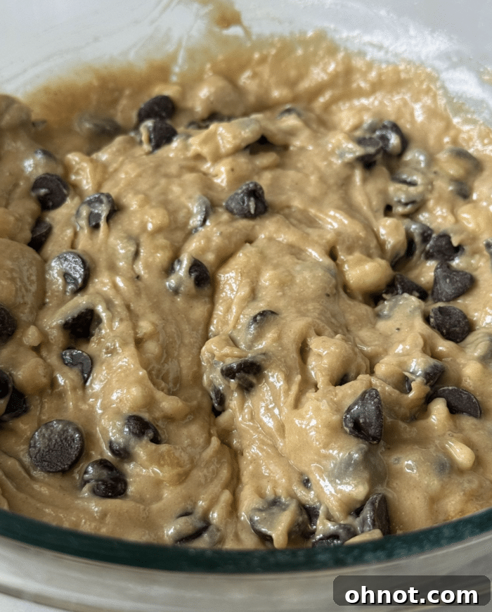 Banana blondie batter in a clear glass bowl, with chocolate chips folded in.