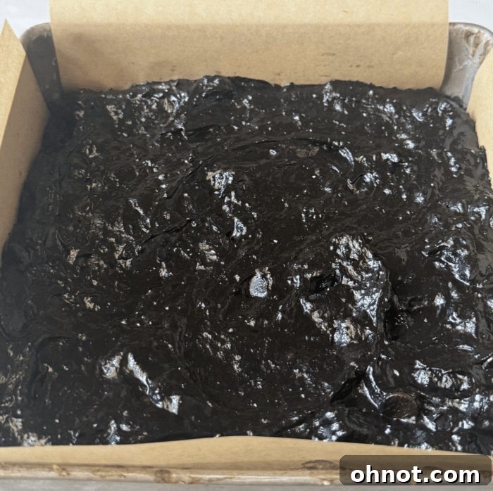 Dark brownie batter spread into a parchment-lined baking pan.