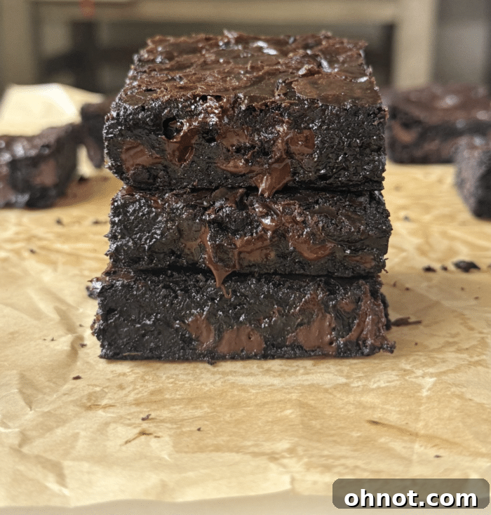 Fudge gooey brownies. A close-up of a pan of cooling, uncut fudgy brownies, showing their rich, dark color and soft texture, with the parchment paper lifting them slightly from the pan.
