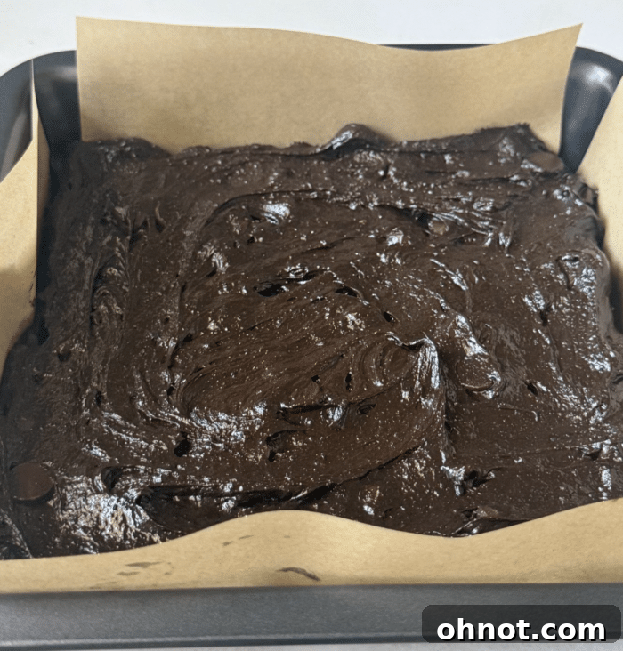 Chocolate batter in pan. The rich espresso brownie batter spread evenly in a parchment-lined baking pan, glistening and ready for the oven to transform.