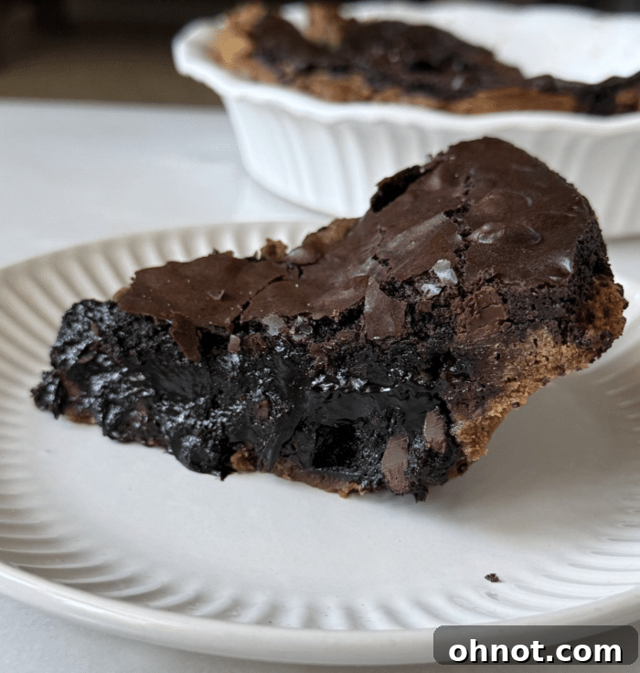Slice of gooey brownie pie on a white plate, showcasing its rich layers.