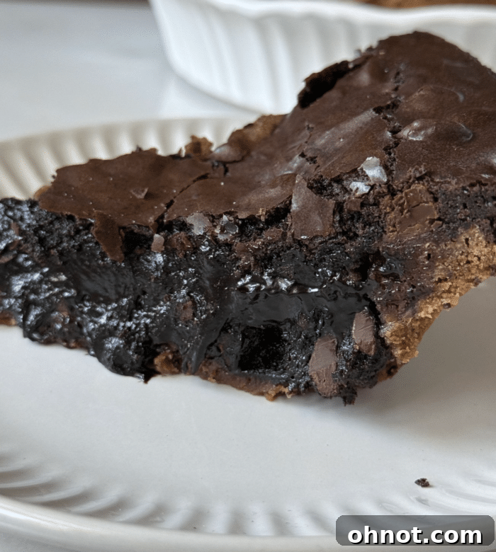 Close-up of a generous slice of gooey brownie pie with a cookie crust, ready to be enjoyed.