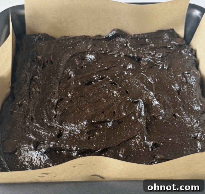 Brownie batter evenly spread in a parchment-lined square baking pan, ready for the next layer.