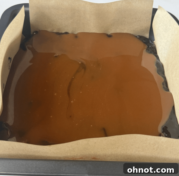 Thick caramel sauce poured over a layer of brownie batter in a baking pan, creating a rich filling.