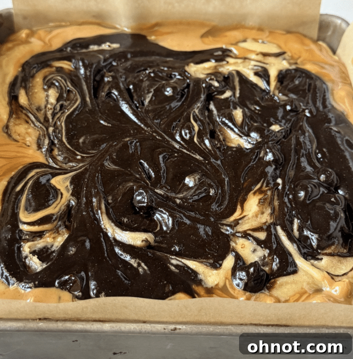 Caramel and peanut butter swirled over a brownie base with peanuts, prior to adding more brownie batter for Snickers Brookies.