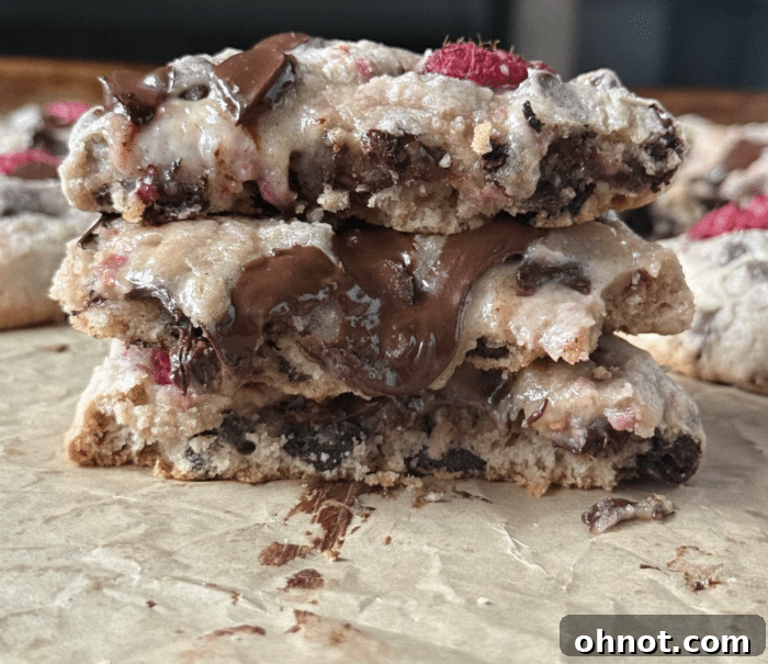 A close-up stack of warm raspberry chocolate chip cookies, showing their gooey centers and fresh raspberries.