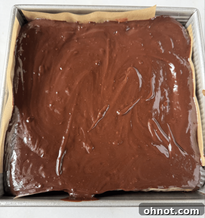 Chocolate ganache evenly spread over a square cheesecake in a pan, chilling.