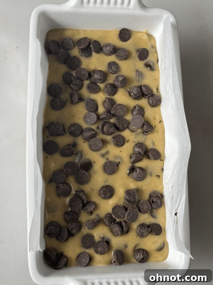 Banana bread batter with visible chocolate chips, ready for layering in a loaf pan.